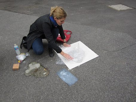 Eine Frau kniet auf dem Boden und arbeitet an einer Zeichnung auf Papier.