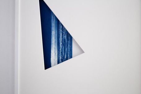 Dreiecksformausschnitt einer weißen Wand, dahinter blauer Himmel und Wellen.