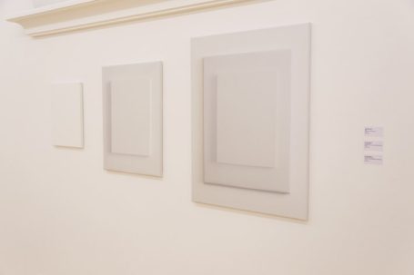 Drei gerahmte, weiße Bilder mit unterschiedlichen Mustern an einer hellen Wand.