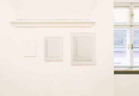 Drei leere, gerahmte Bilder an einer hellen Wand neben einem Fenster.