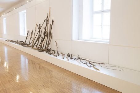 Holzstücke in einer modernen Galerie, arranged entlang einer weißen Wand.