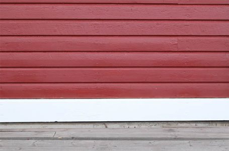 Rote Holzschuppenwand mit weißen Verkleidungen am unteren Rand.