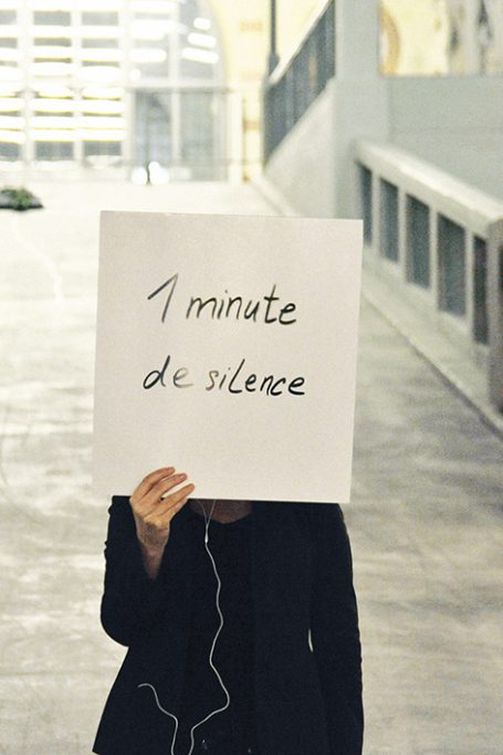 Eine Person hält ein Schild mit der Aufschrift „1 minute de silence“.