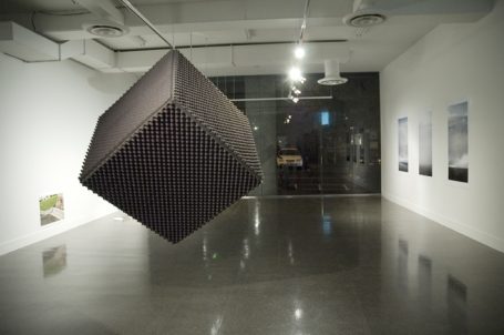 Dunkelgrau schwebendes Objekt in einem modernen Ausstellungsraum, umgeben von Bildern.