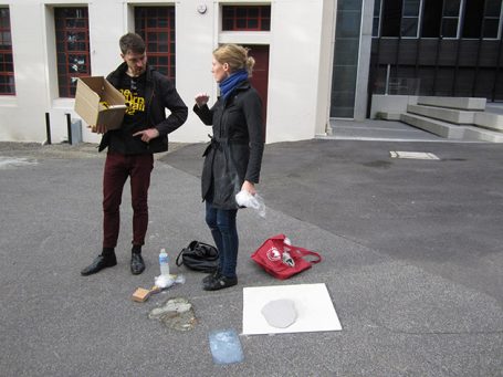 Zwei Personen stehen im Freien, eine hält einen Karton, die andere einen Becher.