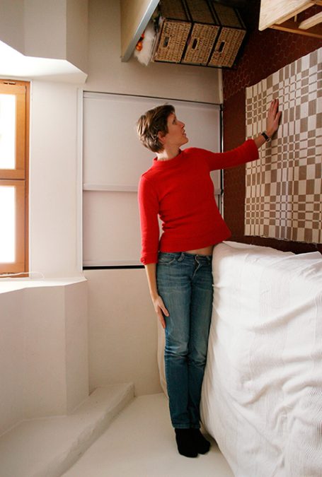 Frau in rotem Pullover zeigt auf eine dekorative Wand mit einem Muster.