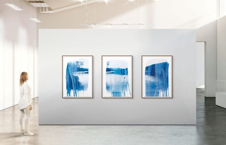 Person betrachtet drei blaue Aquarelle in einem modernen Ausstellungsraum.