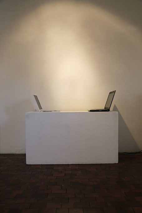 Zwei Laptops auf einem weißen Tisch vor einer hellen Wand.