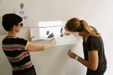 Zwei Frauen arbeiten an einem transparenten Projektionselement an einer Wand.