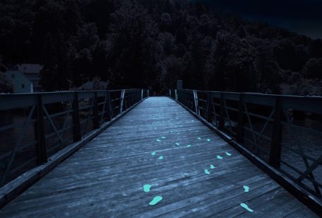 Holzbrücke bei Nacht mit leuchtenden Fußspuren auf dem Boden.