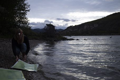 Eine Person legt grüne Matten am Ufer eines ruhigen Sees bei Dämmerung aus.